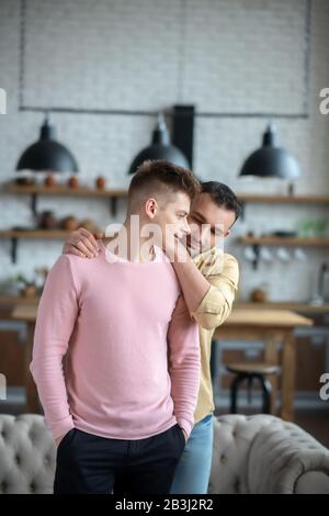 Uomo dai capelli scuri in camicia arancione che abbraccia il suo compagno Foto Stock