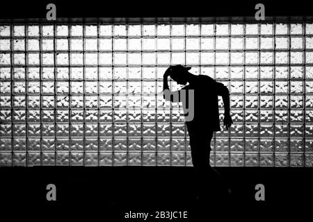 Silhouette retroilluminata di un adolescente che si posa contro il muro di piastrelle di vetro. Tasto shot basso Foto Stock