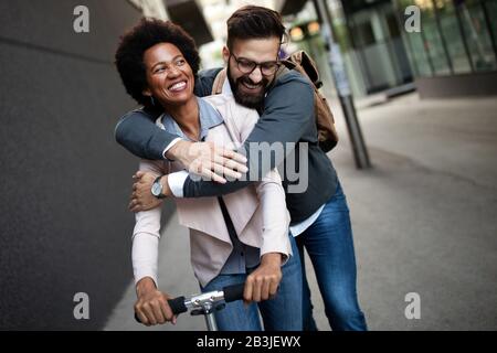 Felice giovane coppia godendo insieme mentre si guida scooter elettrici sulla strada della città Foto Stock