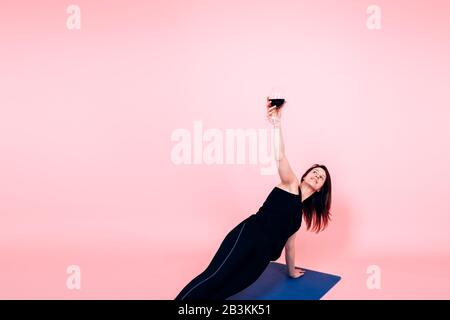 giovane donna che tiene un bicchiere di vino rosso mentre si esegue yoga - vino e yoga tendenza concetto Foto Stock