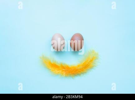 Divertente volto sorridente di due uova di Pasqua di pollo su uno sfondo blu chiaro. Felice Pasqua minimalismo carta da parati, piatto lay Foto Stock