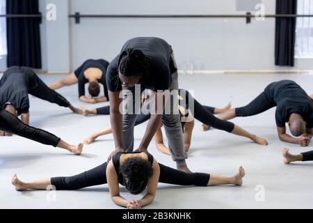 Ballerina maschile che aiuta i ballerini moderni a allungarsi in uno studio Foto Stock