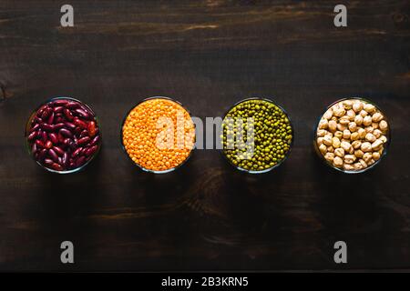 Set di cereali e legumi diversi in una ciotola di vetro su un tavolo nero, vista dall'alto. Concetto di alimentazione sana. Fagioli, ceci, lenticchie e mung b Foto Stock