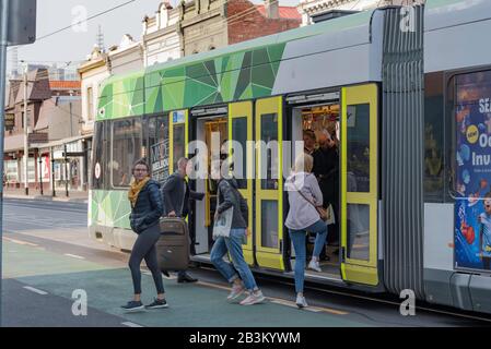 La gente parte, scendendo da (scendendo) un moderno tram di Melbourne dirigendosi lungo Brunswick Street, Fitzroy a Victoria, Australia la mattina. Foto Stock