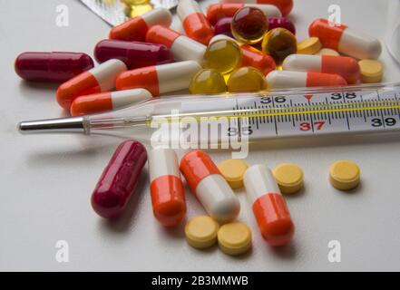 Termometro e pillole - questa composizione si associa a malattia e terapia. Vari farmaci a colori sono situati sullo sfondo bianco. Foto Stock