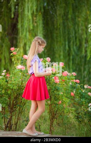 Ritratto di una bella ragazza nel giardino di una rosa tè in primavera. Bella ragazza sorridente bambino con capelli biondi. Foto Stock