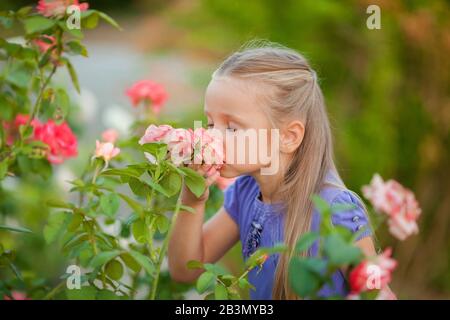 Ritratto di una bella ragazza nel giardino di una rosa tè in primavera. Bella ragazza sorridente bambino con capelli biondi. Foto Stock