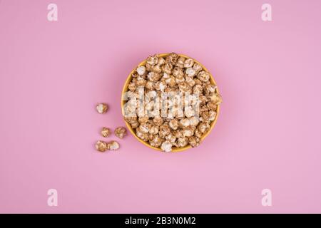 Dolce caramello popcorn recipiente isolato su sfondo rosa vista dall'alto. La composizione della struttura con copia spazio. Foto Stock