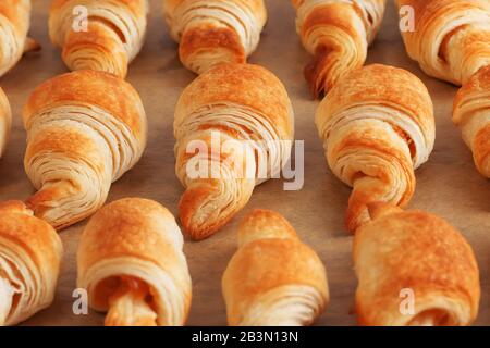 Vista laterale di tre file di croissant dorati appena sfornati di pasta sfoglia con profondità di campo poco profonda con marmellata su carta da forno marrone Foto Stock