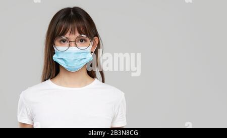 Donna asiatica sensazione di malessere e indossare maschera protettiva viso su sfondo grigio studio. Copiare lo spazio per il testo. La prima difesa contro l'epidemia di Foto Stock