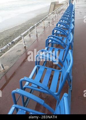 Una fila di sedie a sdraio blu in metallo che si affacciano sui mari tempestosi sulla Promenade des Anglais a Nizza, marzo 2020 Foto Stock