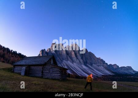 Uomo che ammira le stelle sopra l'Odle da capanna di legno a Gamben Alm, Val di Funes, Dolomiti, provincia di Bolzano, Alto Adige, Italia, Europa Foto Stock