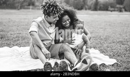 Felice famiglia africana divertirsi durante il fine settimana nel parco pubblico - madre e padre giocare con la loro figlia all'aperto Foto Stock