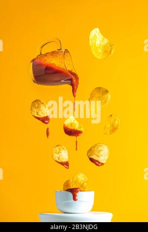 Salsa in vaso di vetro e patatine saporite che cadono nel colpo con ketchup di pomodoro congelato nell'aria. Versare una cassella di pomodoro calda in scatola fai da te fatta in casa Foto Stock