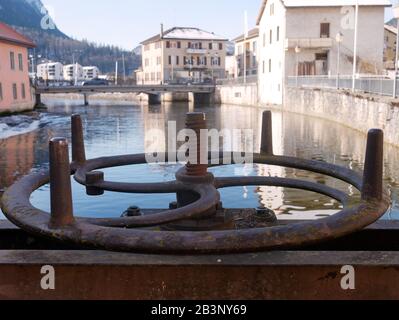Primo piano della vecchia valvola a saracinesca arrugginita. Edifici e il ponte del villaggio, e la montagna sullo sfondo. Foto Stock