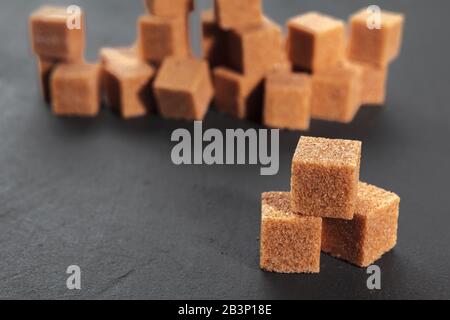 Cubetti di zucchero marrone naturale su fondo nero ruvido Foto Stock