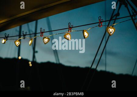 Fata luci in forma di cuore su uno yacht vicino alla costa. Vela romantica, yachting e concetto valentine. Foto Stock