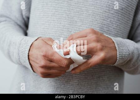 vestirsi di un uomo caucasico, indossando un maglione casual grigio chiaro, disinfettando le mani con una salvietta bagnata Foto Stock