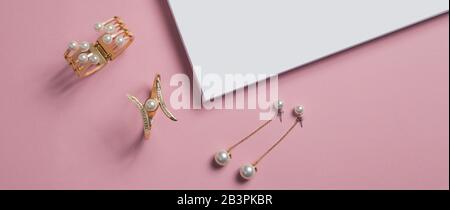 Vista dall'alto di bracciali e orecchini dorati su sfondo di carta rosa e bianca Foto Stock