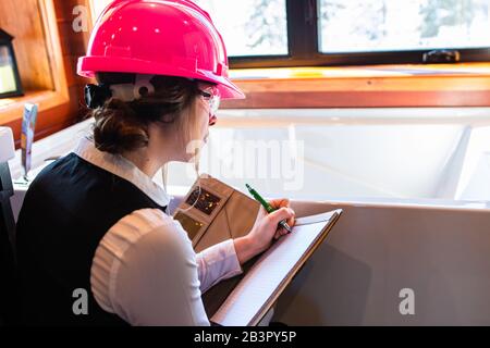 Vista posteriore di ispettore di costruzione femminile alla ricerca di stampi o funghi problemi sul bagno e prendere appunti durante l'ispezione di qualità dell'aria interna Foto Stock