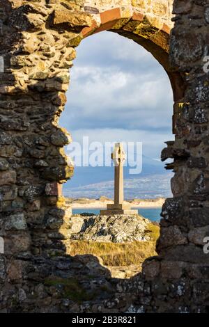 La croce celtica guardò attraverso le rovine della chiesa di St Dwynwen sull'isola di Llanddwyn, Anglesey, Galles Foto Stock