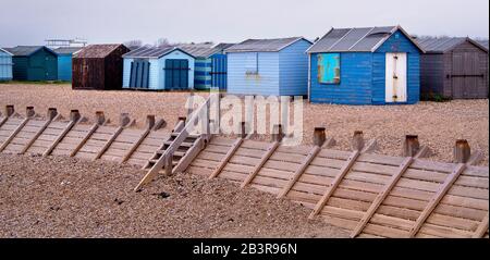 Colorate capanne sulla spiaggia di ghiaia con un frangiflutti di fronte Foto Stock