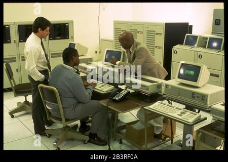 Austin Texas USA,1990: Supervisor guarda il lavoro di specialista di immissione dati sul terminale di computer con computer mainframe in background a un processo c Foto Stock