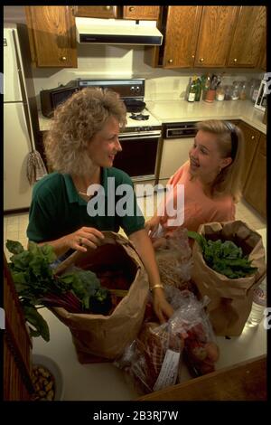 Austin Texas USA, circa 1990: Anglo madre e pre-teen figlia prendere generi alimentari da borse shopping nella loro cucina dopo lo shopping al negozio di alimentari. ©Bob Daemmrich Foto Stock