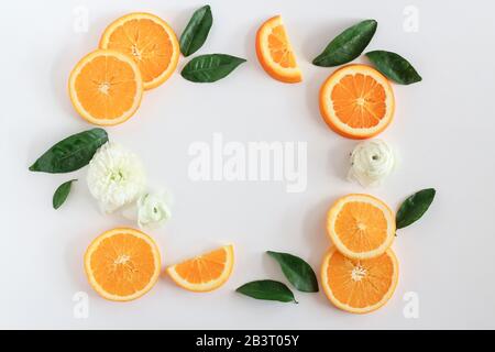 Una cornice fatta di fette, foglie e fioriture arancioni su uno sfondo bianco con uno spazio di copia Foto Stock