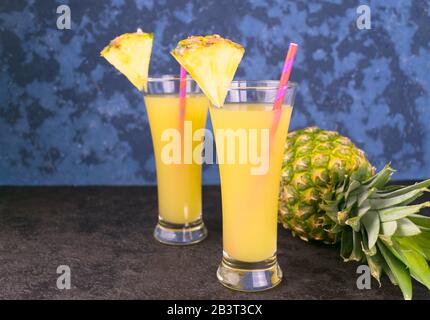 Due bicchieri di succo di ananas fresco e ananas su sfondo blu. Spazio di copia. Foto Stock