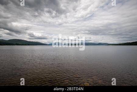 Loch Lomond, Scozia. Una vista ad ampio angolo sulle acque delle sponde meridionali del Loch Lomond adagiato contro un cielo grigio tempestoso. Foto Stock