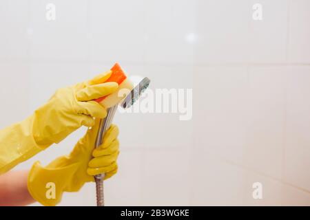 Donna in guanti di gomma che puliscono il soffione della doccia. Lavatrice domestica con testa metallica della doccia. La cameriera si pulisce in bagno Foto Stock