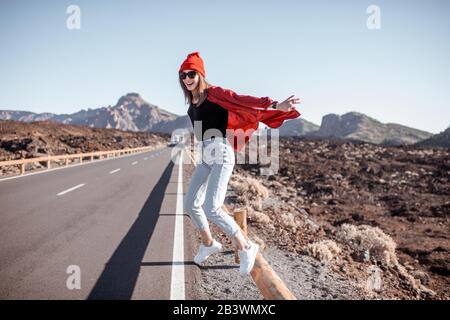 Ritratto lifestyle di una giovane donna elegantemente vestita di salto rosso sulla strada, viaggiando sulla valle vulcanica in una giornata di sole. Stile di vita spensierato e concetto di viaggio Foto Stock