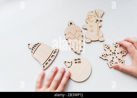Giocattoli di legno in mani di capretto, pronti per fare ornamenti dell'albero di Natale di legno su sfondo bianco.ornamenti di Natale domestici. Hobby, fai da te Foto Stock