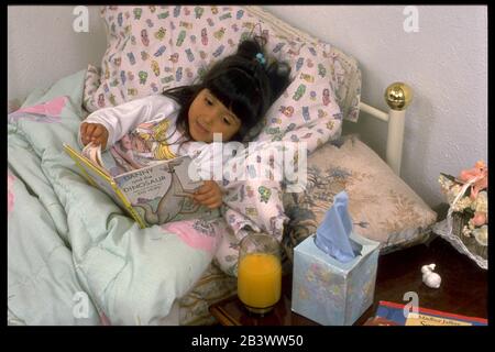 Austin, Texas USA: Ragazza di sette anni che soffre di un freddo mite bevendo un bicchiere di succo d'arancia a letto prima di andare a dormire. ©Bob Daemmrich Foto Stock