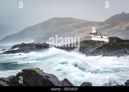 Mari tempestosi e alte onde che si infrangono sulle rocce di fronte al faro di Valentia nella contea di Kerry Irlanda Foto Stock