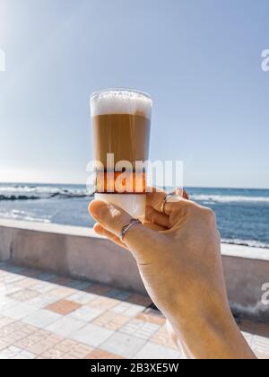 Tenere il tradizionale caffè delle canarie barakito sullo sfondo del mare. Immagine realizzata sul telefono cellulare Foto Stock