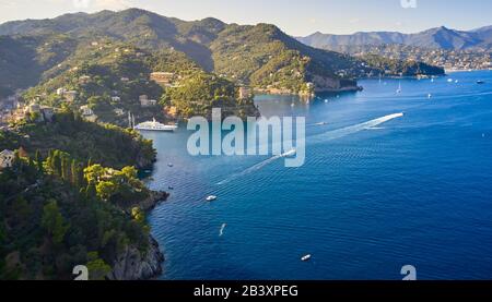 Barche e barche navigano nel Mar Ligure sullo sfondo della montagna, Portofino, Italia. Rocce e colline al mare con la tradizionale italiana Foto Stock