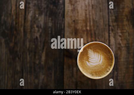 Tazza da caffè con design decorativo in foglia su sfondo rustico in legno - vista dall'alto con spazio per il testo Foto Stock