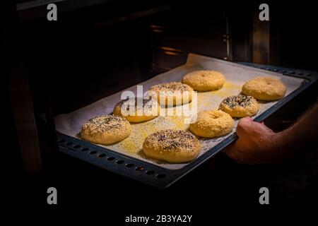 Bagel appena sfornati ricoperti di semi di papavero e sesamo disposti su una teglia da forno e andando in un forno caldo per essere cucinati Foto Stock