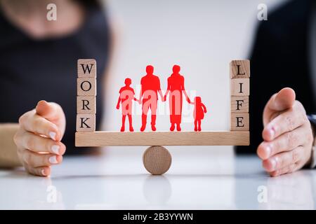 Coppia felice la protezione di equilibrio tra lavoro e vita familiare e carta ritagliata su altalena Foto Stock