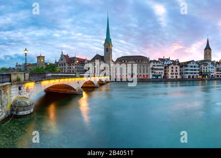 Famosa chiesa Fraumunster e ponte Munsterbrucke sul fiume Limmat al tramonto nel centro storico di Zurigo, la città più grande della Svizzera Foto Stock
