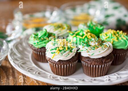 Un piatto di cupcake in miniatura di cioccolato smerigliato verde e bianco decorato con oro, giallo e verde cosparge assortite. Spruzzate sfocate nel dorso Foto Stock