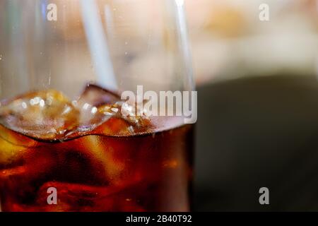 Primo piano e macro vista di cola e ghiaccio cubo con vapore sul vetro, e sfocatura sfondo astratto di bokeh. Foto Stock