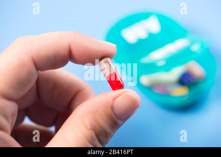 Capsula colorata in mano al paziente con dispenser giornaliero di pillole su sfondo blu. Foto Stock