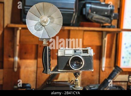 Vecchia fotocamera e riflettore pieghevole flashbulb su treppiede, su sfondo sfocato isolato con percorso di ritaglio. Foto Stock