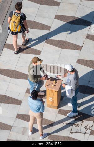 Vista aerea delle persone che scommettono denaro sul gioco di pisello, o tre shell con. Uomo che consegna una nota di 20 euro Foto Stock