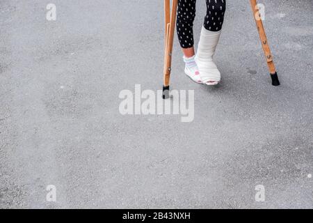 Bambino che usa stampelle e gambe rotte per camminare all'aperto, primo piano. Gamba rotta, stampelle di legno, lesione alla caviglia. Frattura ossea e frattura della caviglia bei Foto Stock