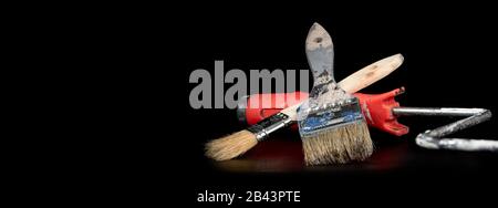 Una spazzola e un rullo di vernice contro uno sfondo nero sotto illuminazione da studio Foto Stock