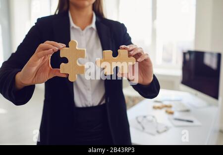 Mani senza volto di una donna d'affari con puzzle in legno in mani in ufficio. Foto Stock